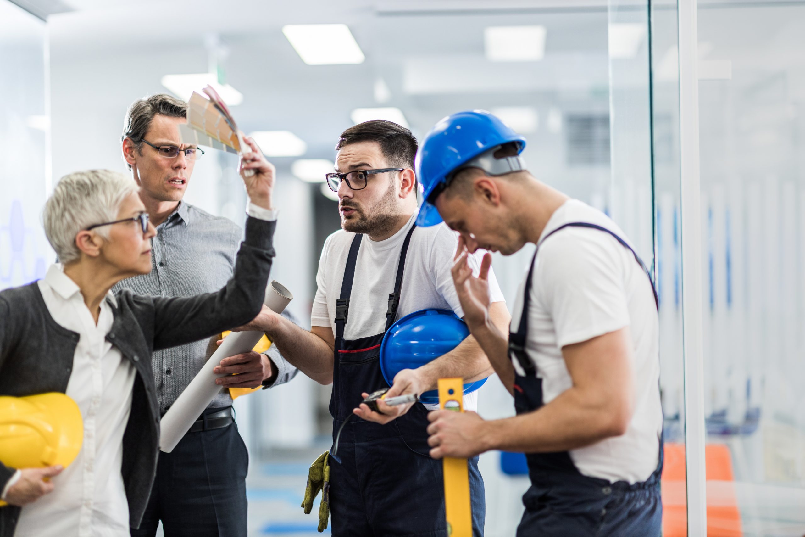 Manual Workers Having Problems With Architects In A Hallway Of An Office Building.